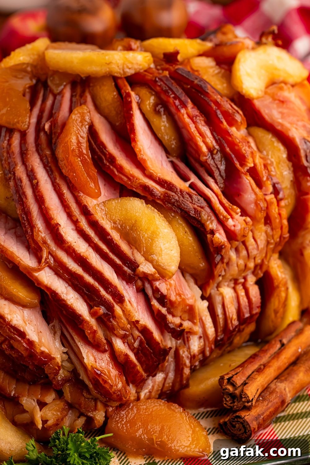 side view of a Slow Cooker Apple Glazed Ham sitting on a platter with cinnamon sticks in front 