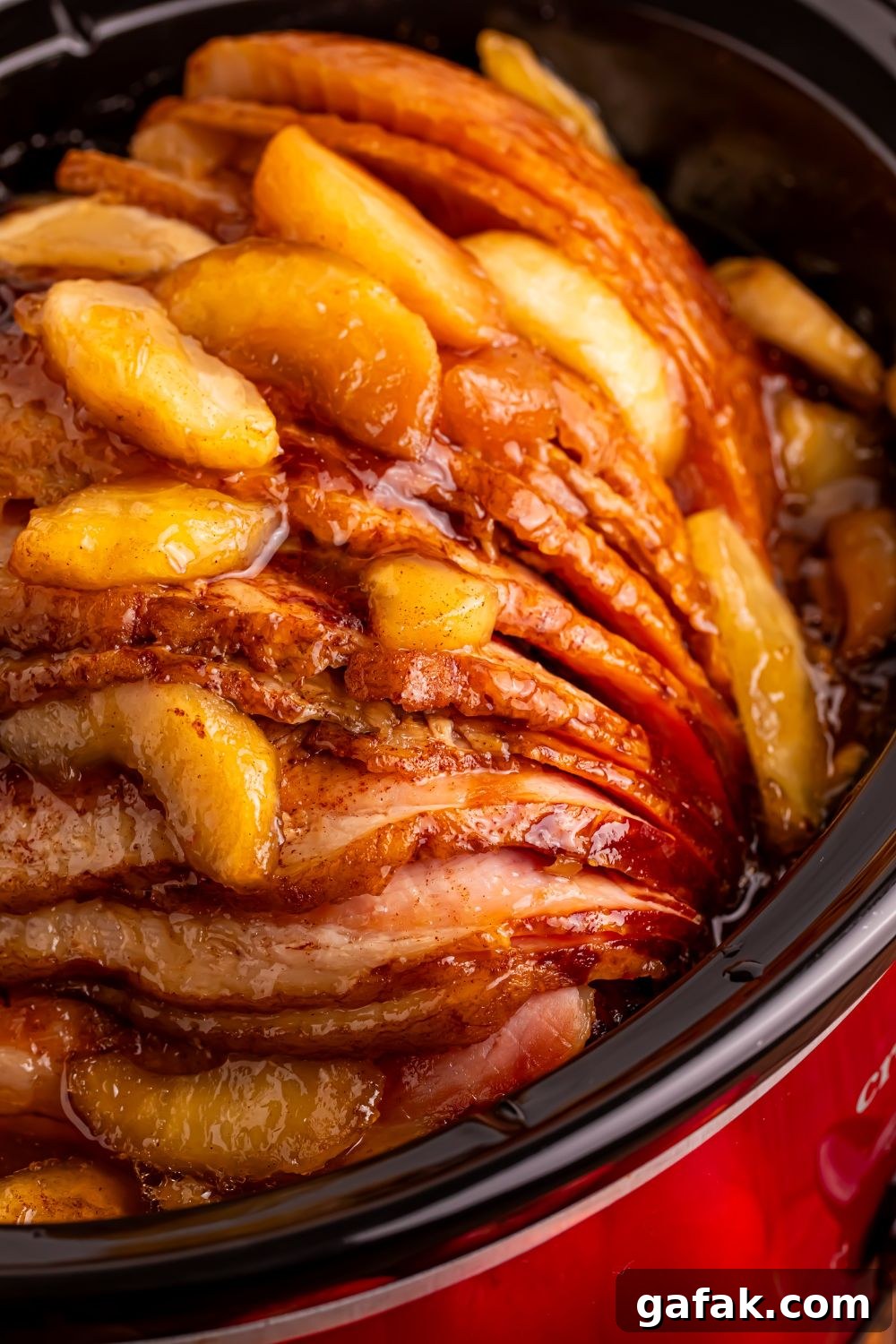 close up look of a red slow cooker with a apple topped spiral ham