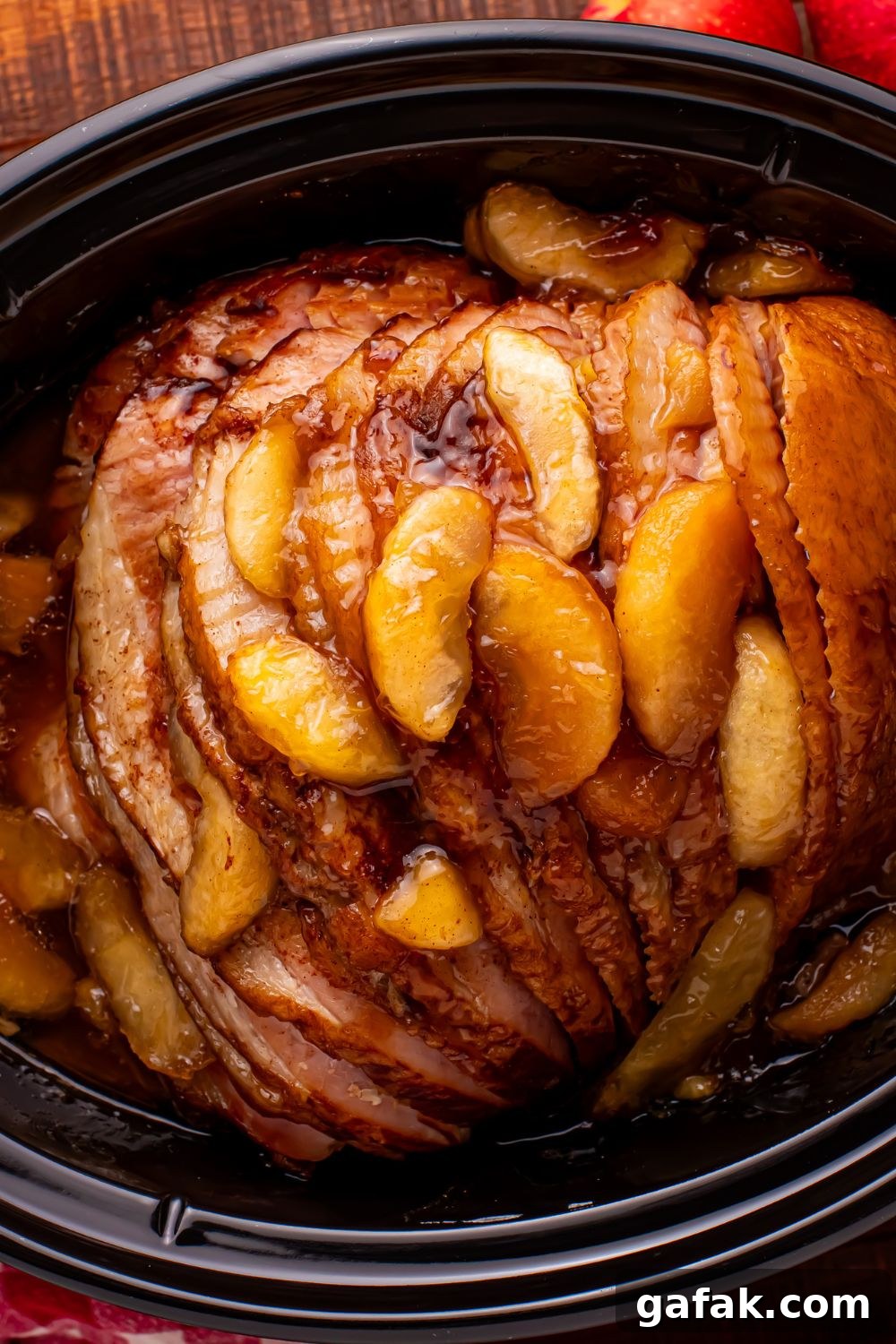looking down at a black slow cooker with a spiral cut ham and baked apples on top of the ham