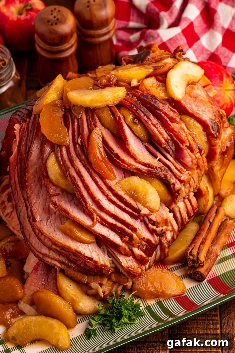 Slow Cooker Apple Glazed Ham on a plaid platter sitting on table with a checkered red towel behind ham, salt and pepper shakers 