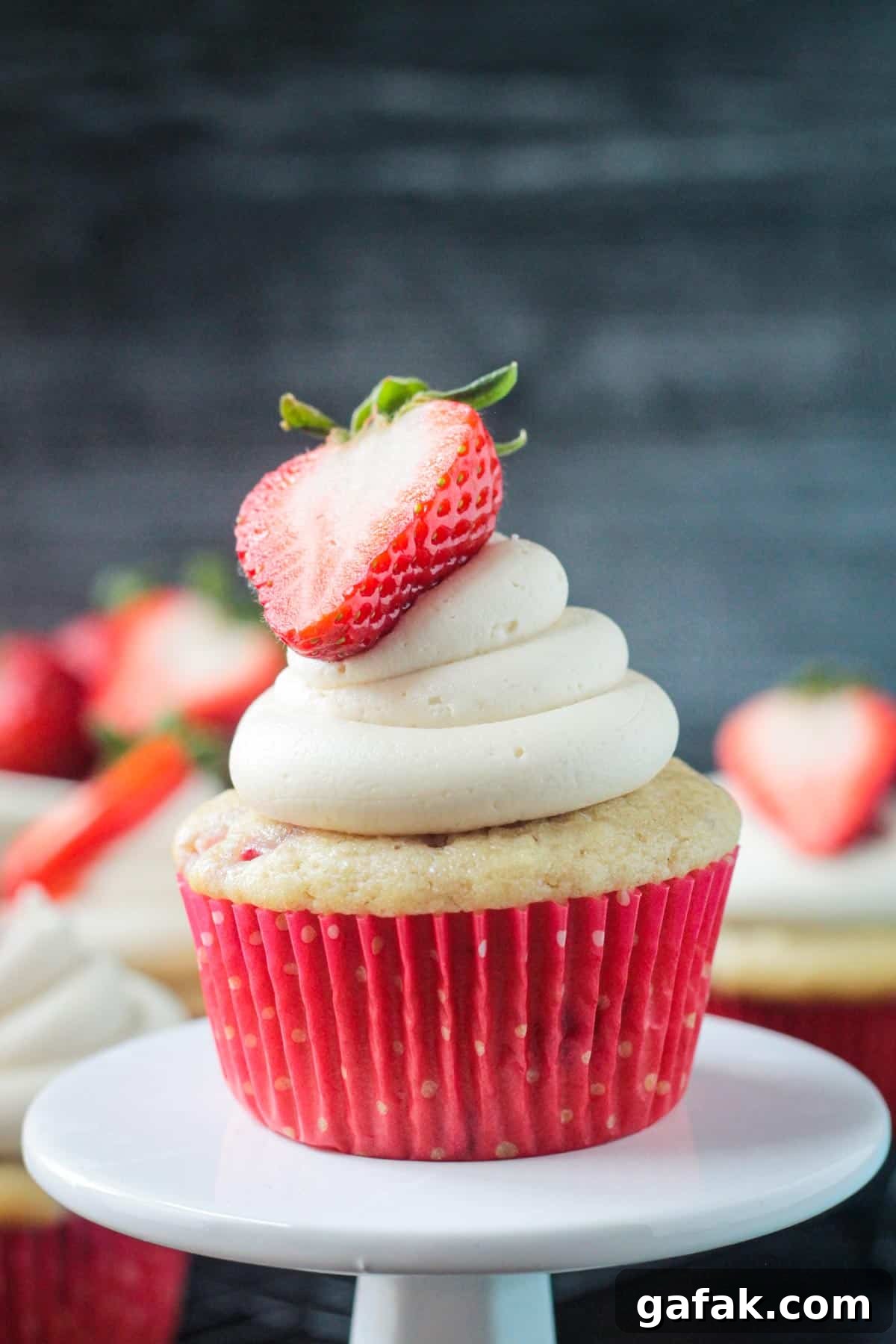 Close up of one vanilla frosted strawberry cupcake in a red paper liner.