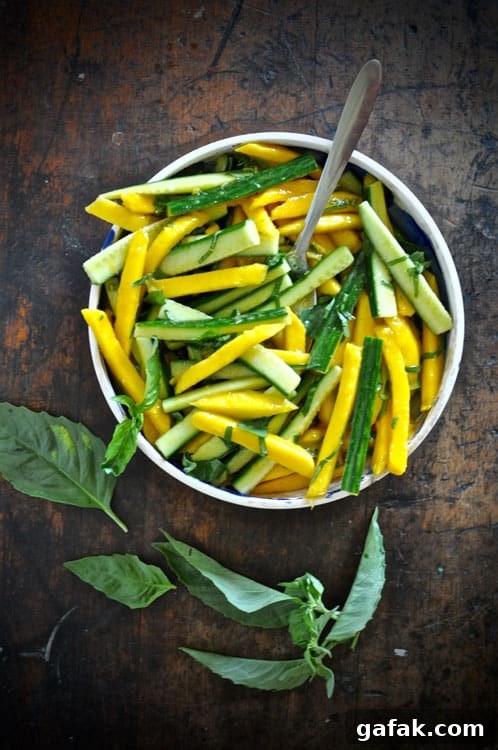 Mango and Cucumber Salad with Spicy Cayenne Dressing 2 A shallow bowl filled with Mango-Cucmber Salad with Cayenne Vinaigrette on a wooden table with basil leaves.