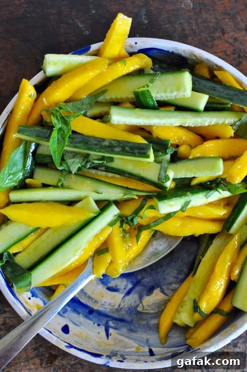 Mango and Cucumber Salad with Spicy Cayenne Dressing 3 Mango-Cucumber Salad arranged in a blue and white bowl sitting on a wooden table with a spoon.