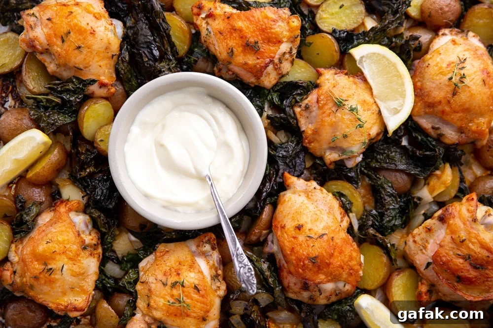 Close up of one pan roasted chicken and veggies with a bowl of aioli and lemon wedges.