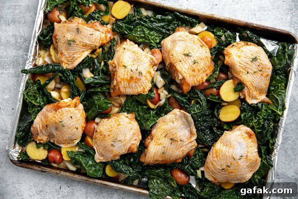 Process shot showing the uncooked chicken thighs over the bed of vegetables on a sheet pan.
