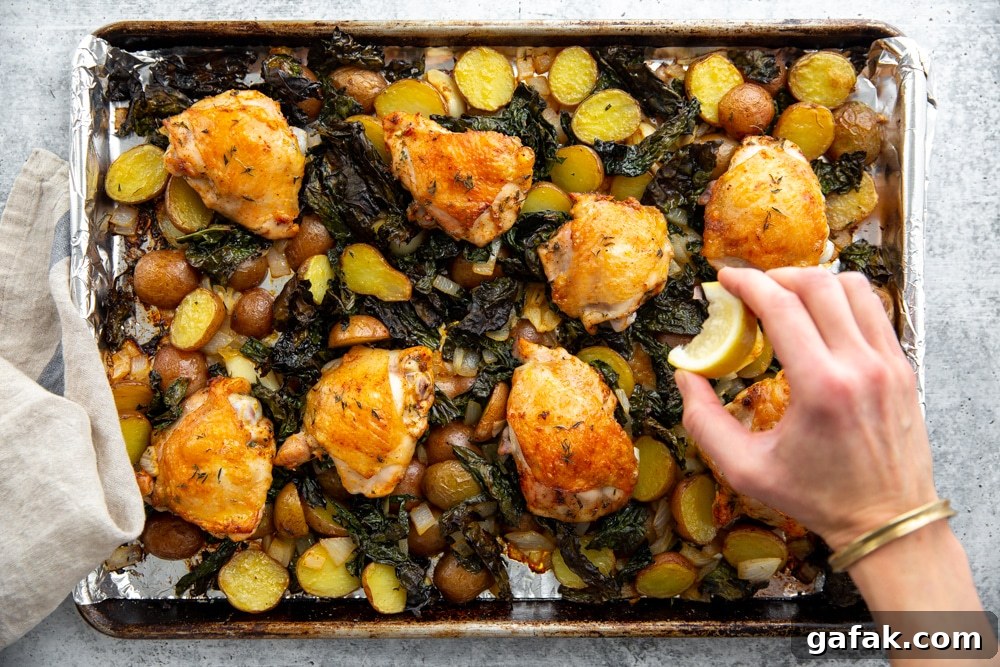 Hand squeezing fresh lemon juice over the one pan chicken and veggies.