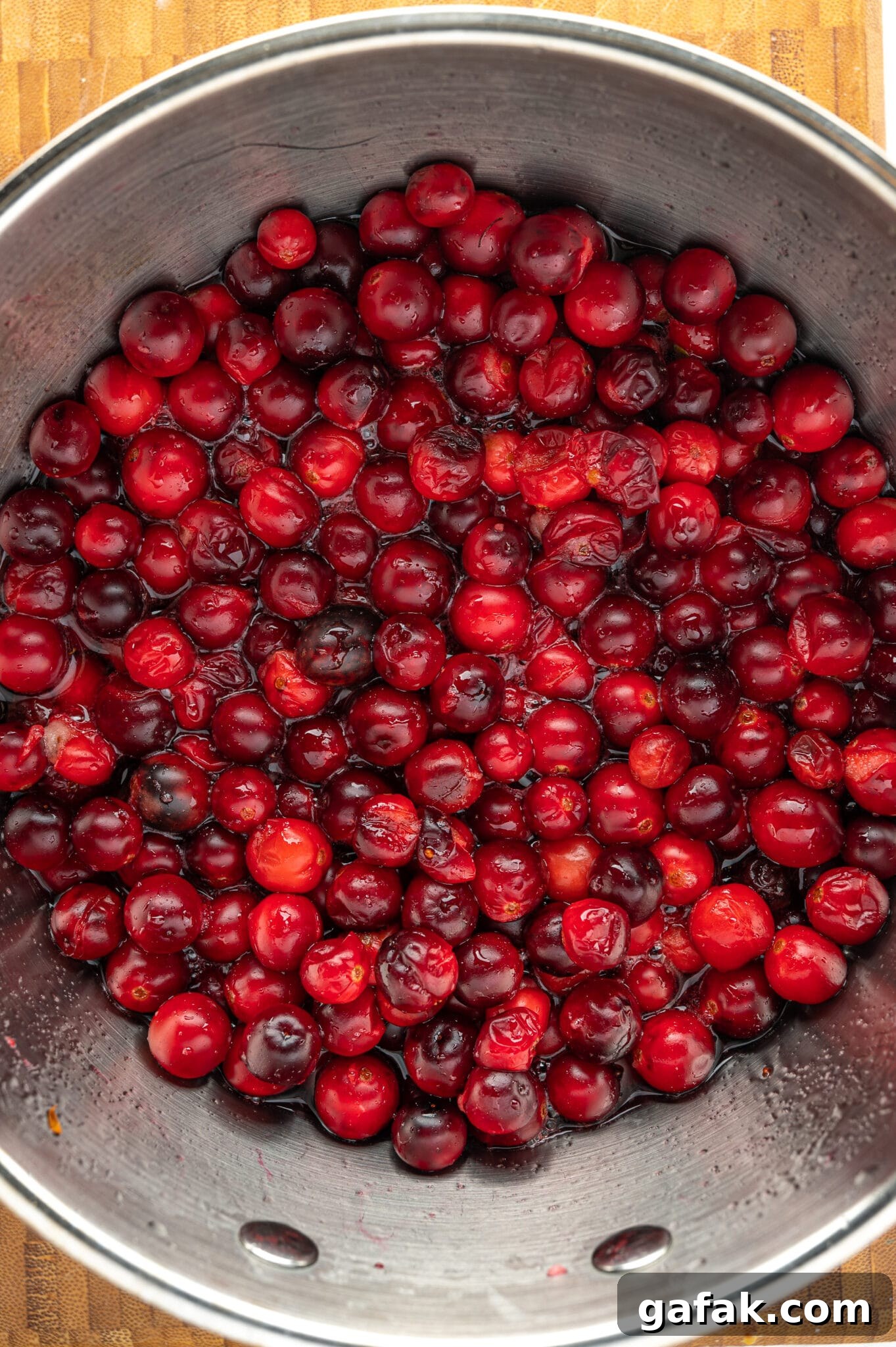 A pot of red ripe cranberries cooking in sugar-free syrup.  A few of the berries have cracked.