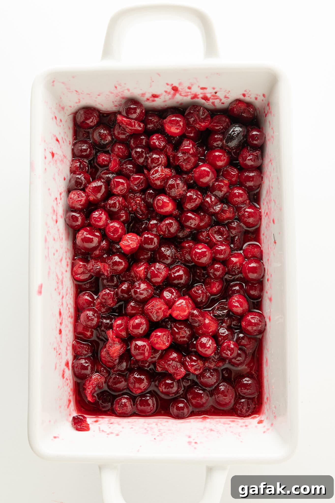 A white dish filled with ruby red berries glossy coated with a thick syrup. 