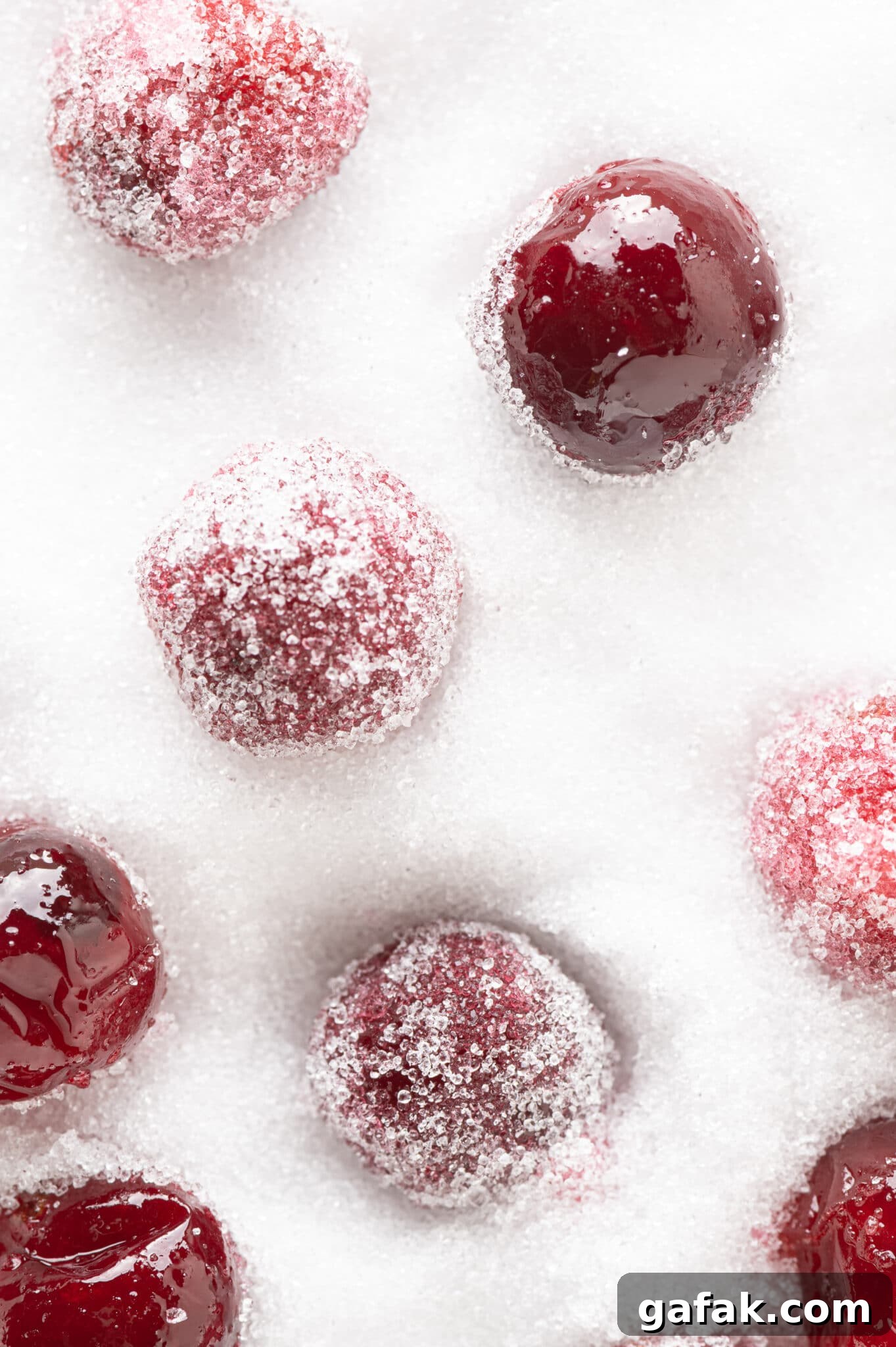 A few coated and uncoated sugar-free candied cranberries sitting in a dish of granular sweetener. 