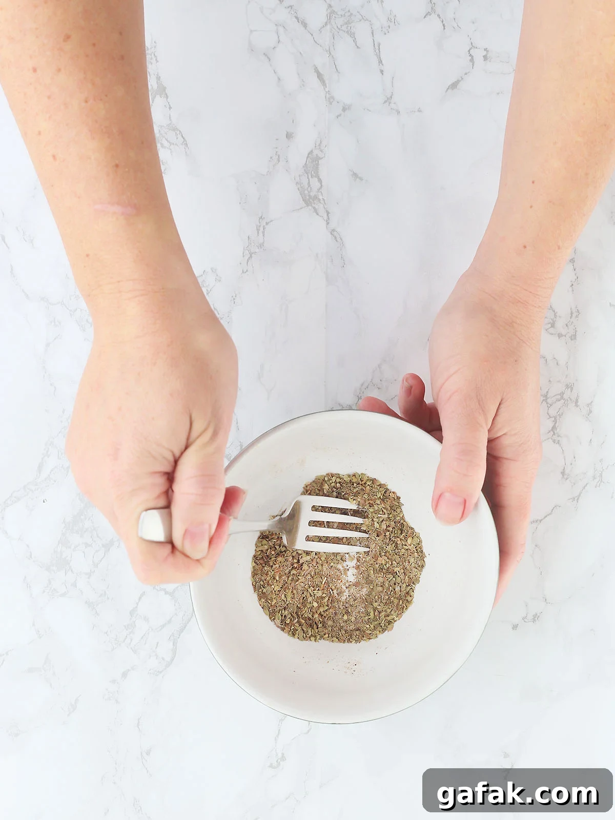 Hand using a fork to mix up the seasoning ingredients in a small mixing bowl.