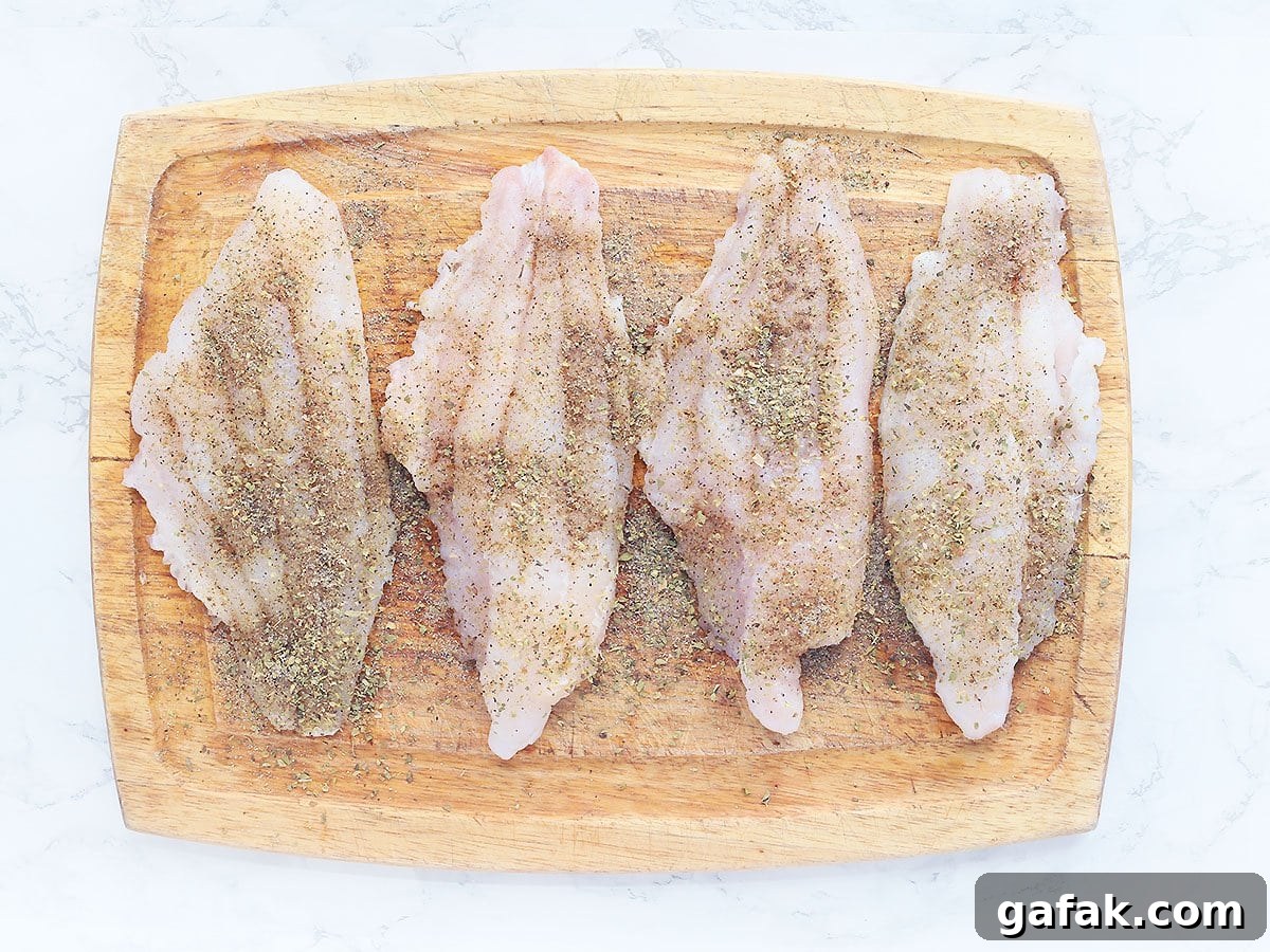 Four seasoned catfish fillets on a wooden cutting board.