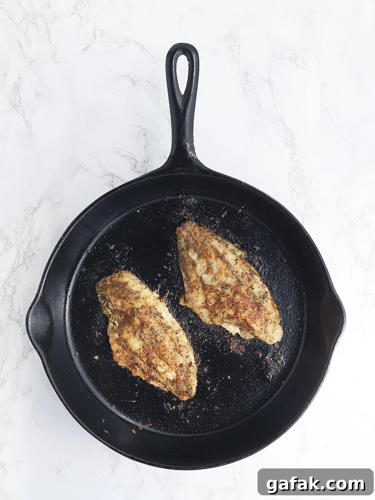 Two catfish fillets in a cast iron skillet after they have been seared on both sides.