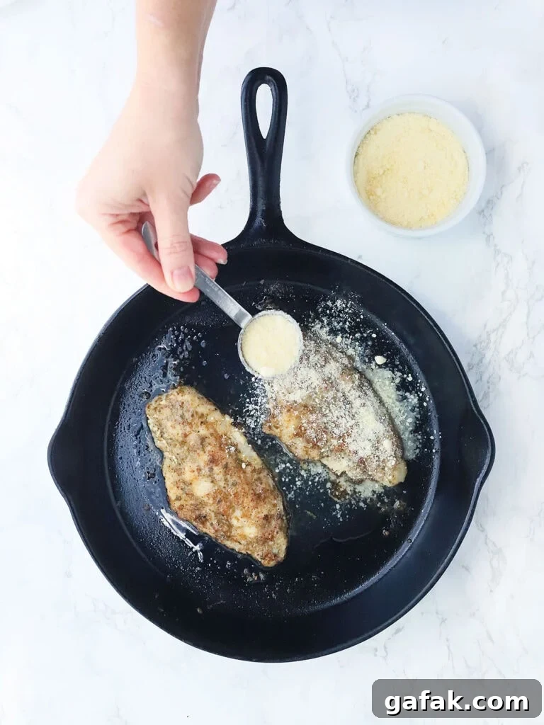 Hand sprinkling Parmesan cheese over two catfish fillets