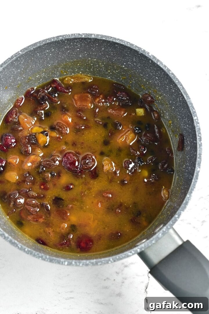 How to Make Gluten-Free Fruit Cake A mixture of dried fruits in orange liquid in saucepan.
