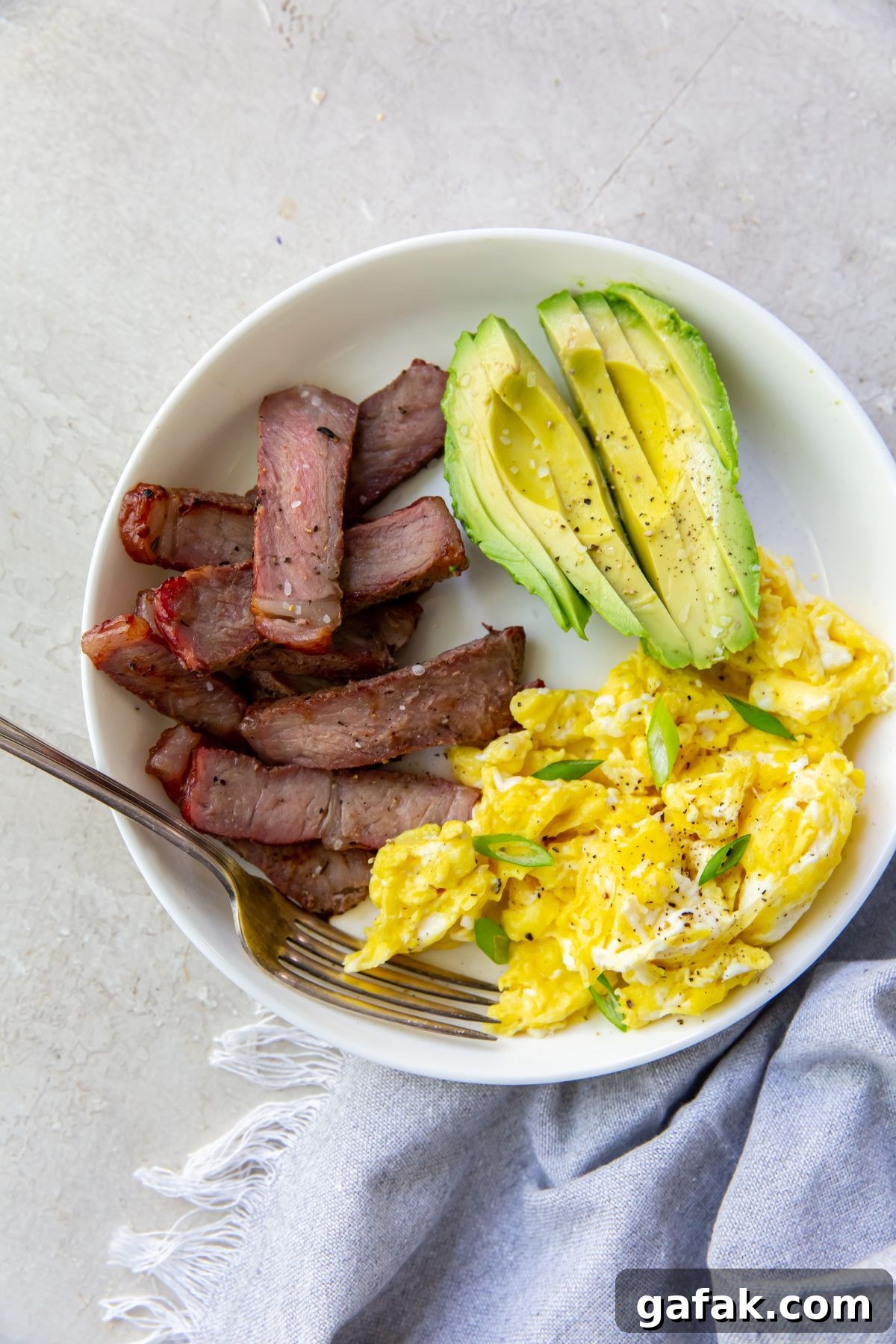 leftover steak breakfast on a white plate with a fork on it and a grey napkin