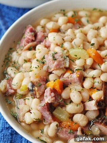 Navy bean and ham soup with celery and carrots served in bowl.