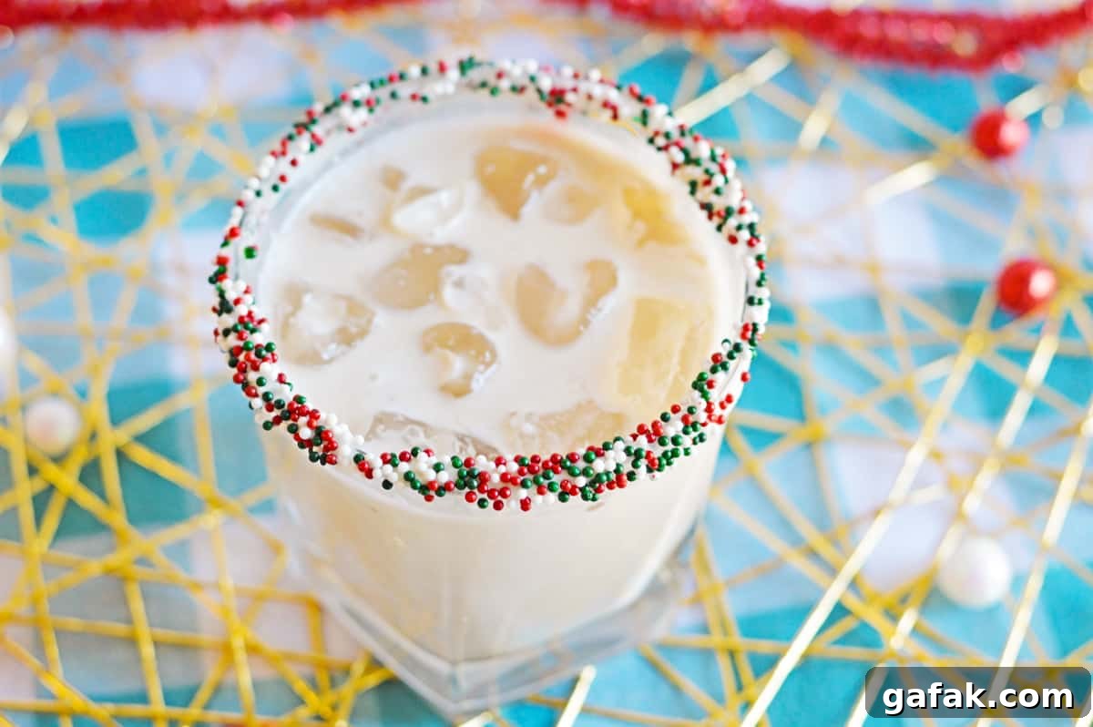 White creamy cocktail in glass with ice and christmas sprinkles on rim
