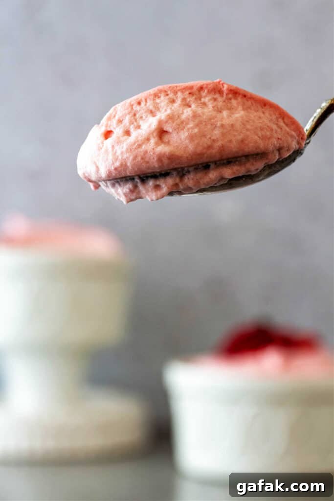 A bite of airy, pale pink strawberry mousse on a spoon.