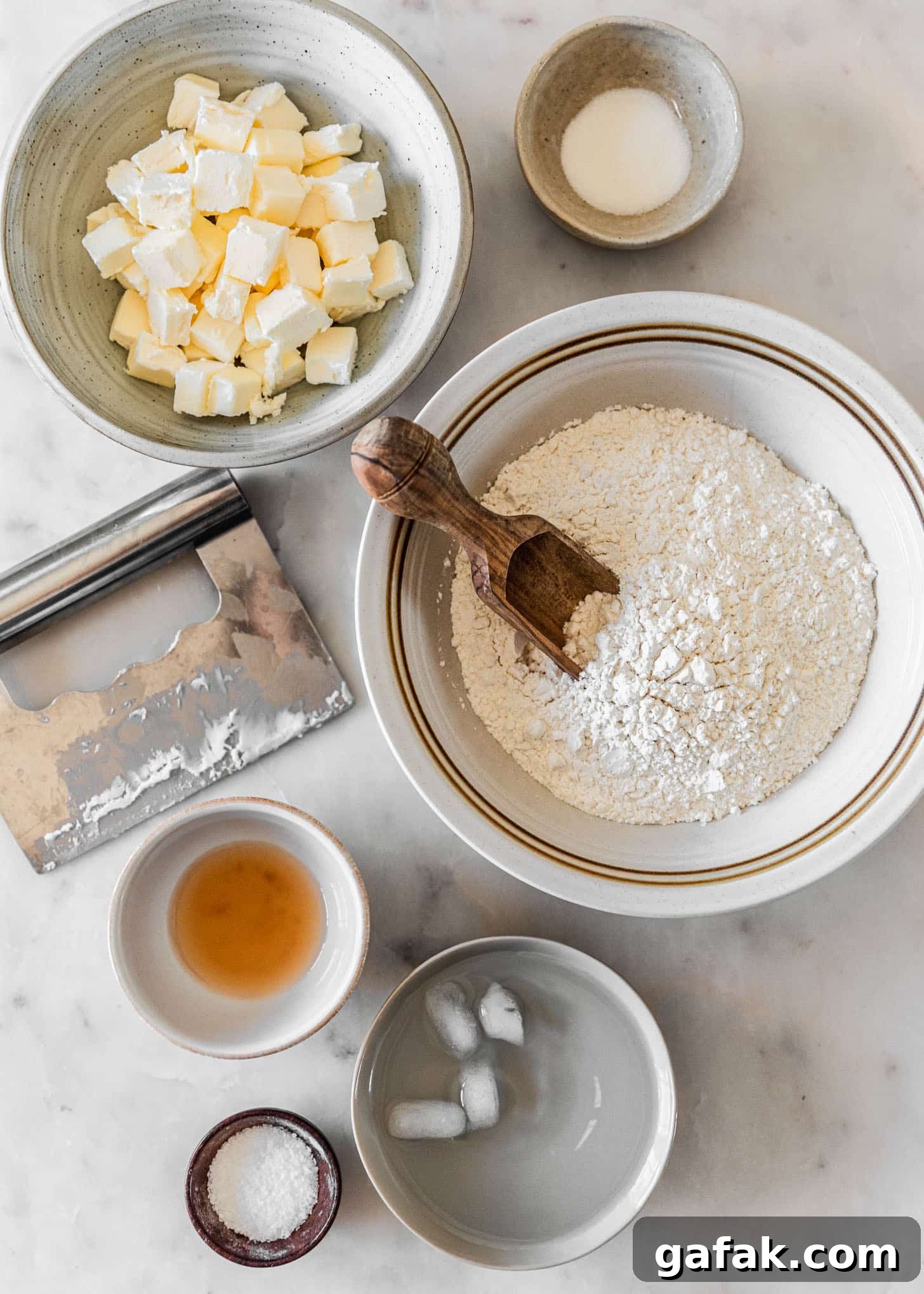 Ingredients for homemade pie dough in white and grey bowls on a white marble counter.