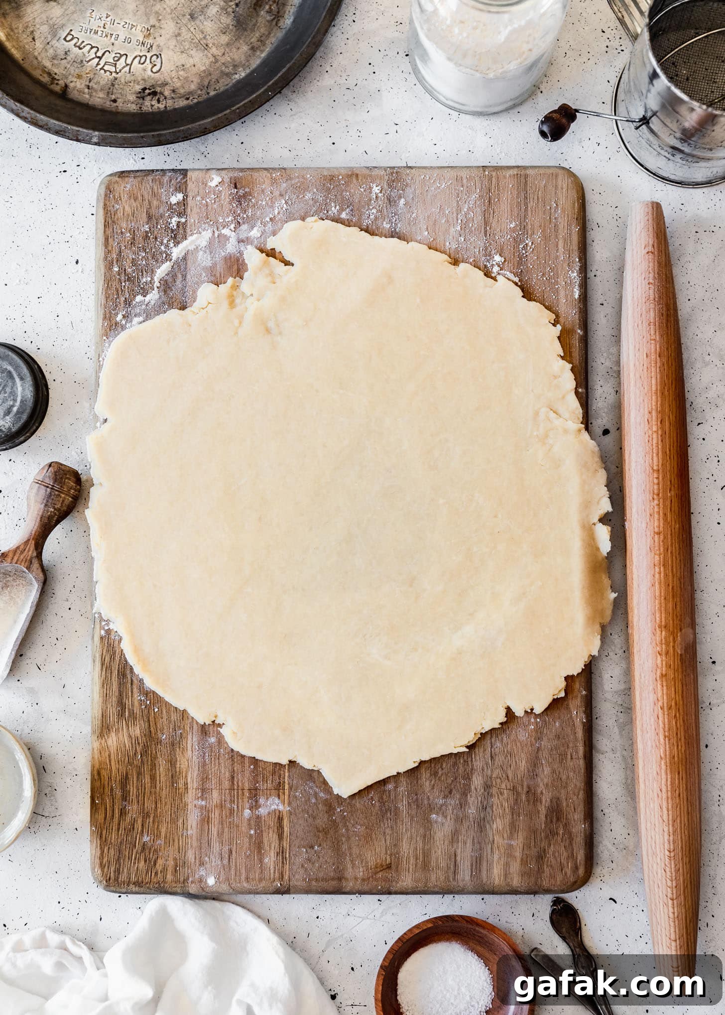The best pie crust rolled out on a wood board next to baking tools and ingredients with a grey background.