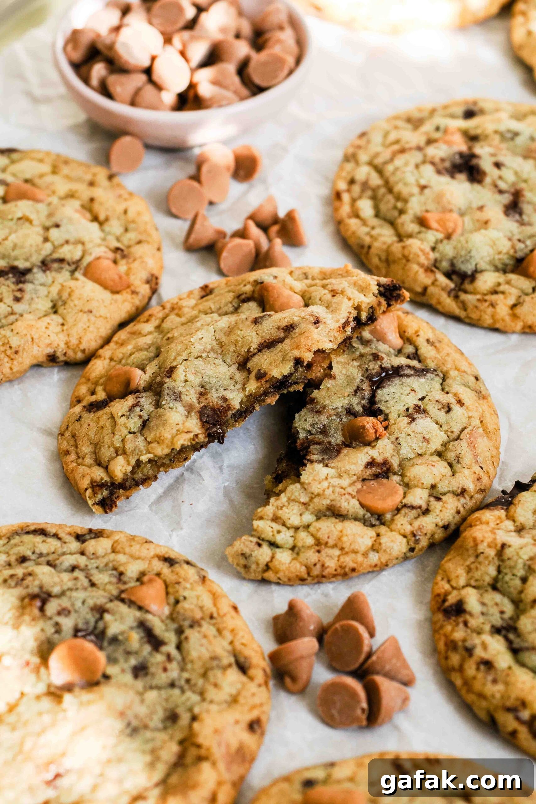 A caramel chocolate chip cookie broken in half on a cookie sheet.