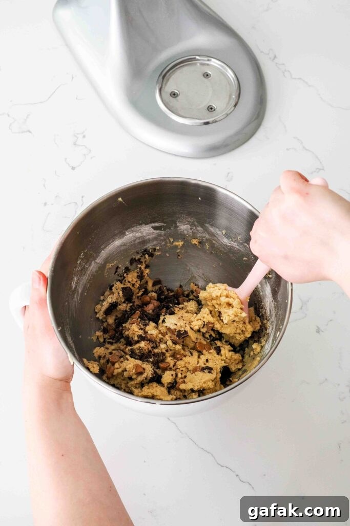 Cookie dough is stirred by hand to incorporate caramel and chocolate chips.