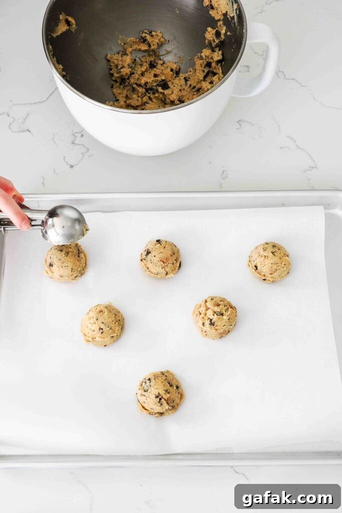 A cookie scoop releases a ball of cookie dough onto a baking sheet.