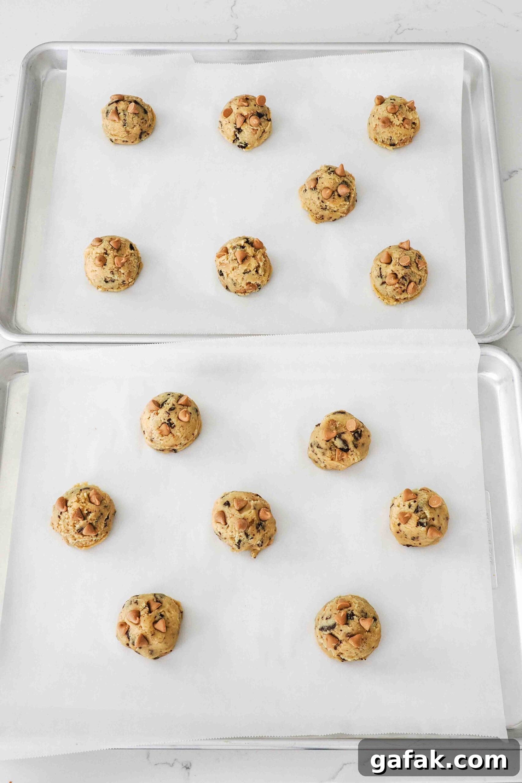 Unbaked caramel chocolate chip cookie dough balls on a baking sheet.