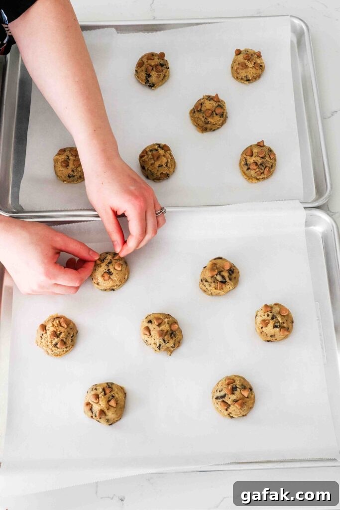 Hands press extra caramel chips into a cookie dough ball.