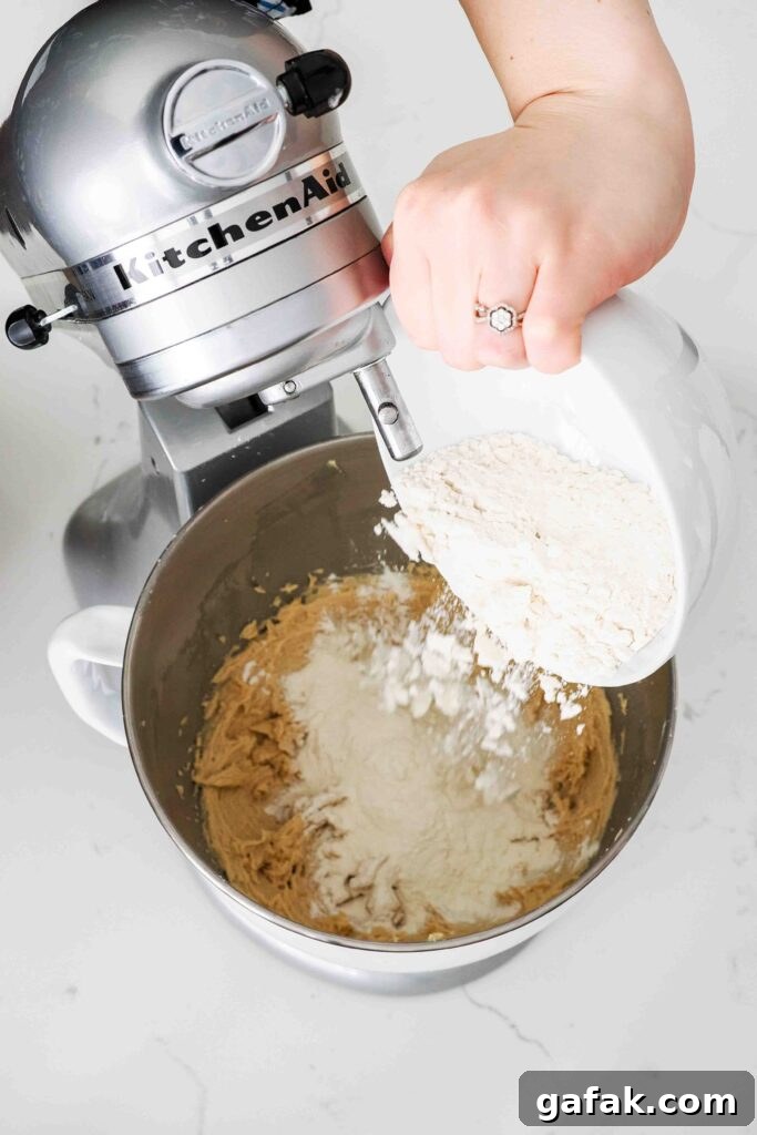 Flour is poured into a stand mixer bowl with creamed butter and sugar.