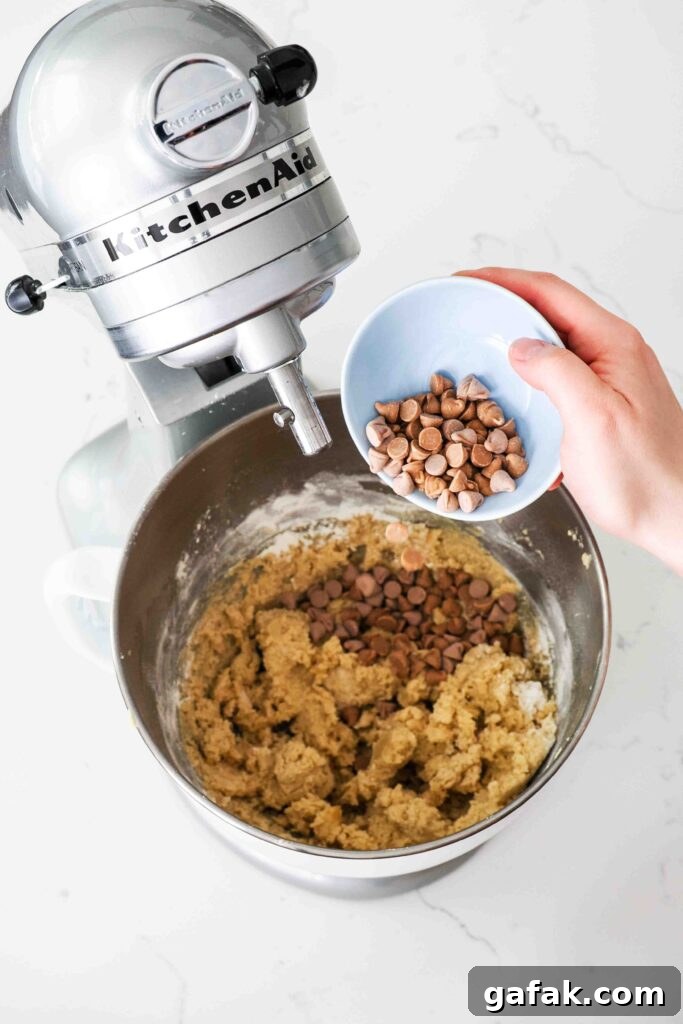 A hand pours caramel baking chips into cookie dough.