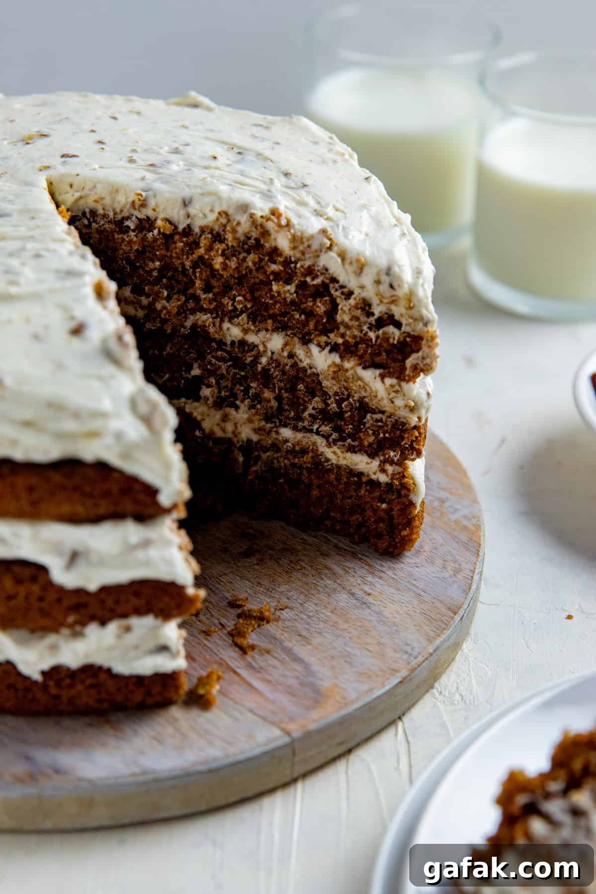 Frosted 3-layer carrot cake with one serving removed on round wooden cake platter.