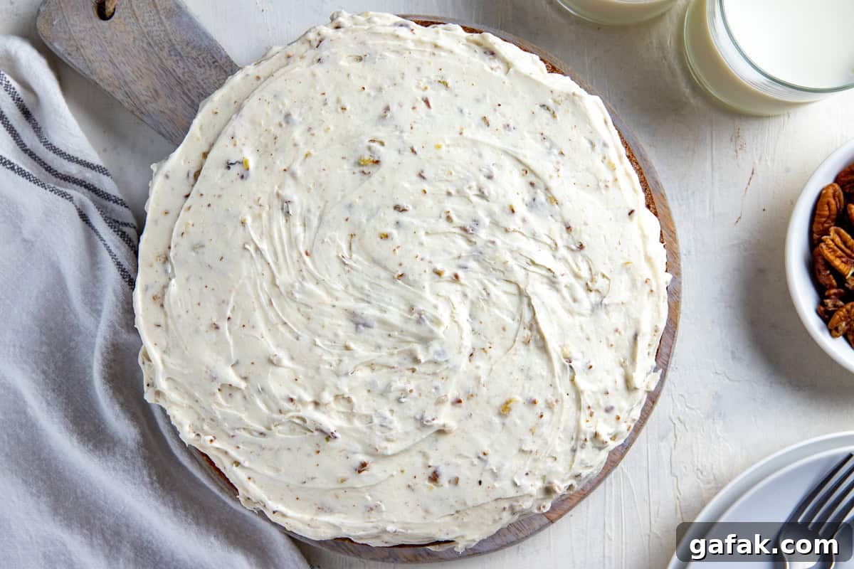 Overhead view of whole frosted carrot cake on round wooden cake platter.