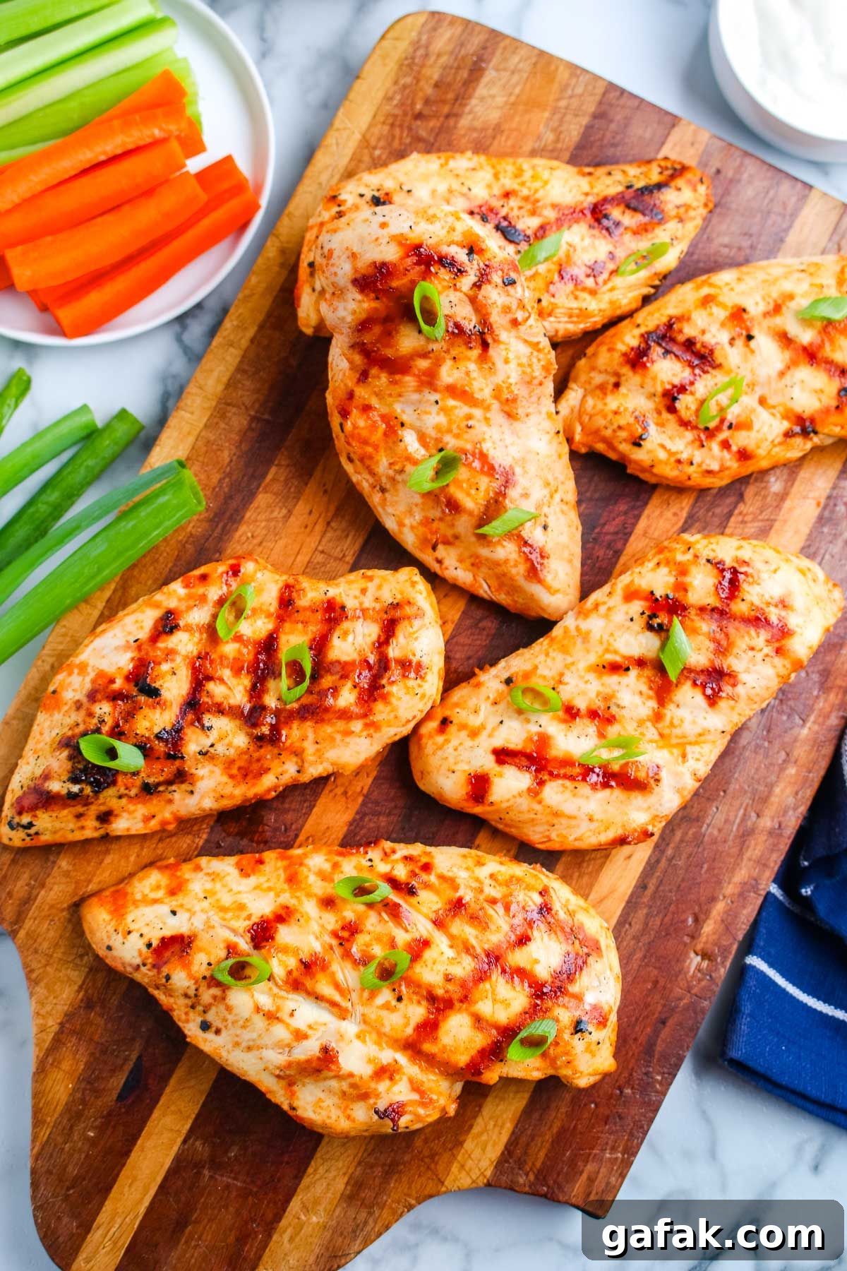 Grilled buffalo chicken breasts arranged on a wooden cutting board with green onions, carrots, celery, and ranch dressing.