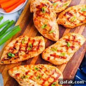 Grilled buffalo chicken breasts arranged on a wooden cutting board with green onions, carrots, celery, and ranch dressing.