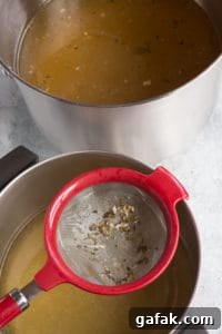 a fine mesh strainer over a pot of turkey stock with the unrefined stock in a pot next to it