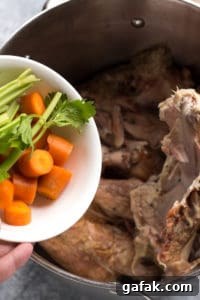 adding cut celery and carrot into a large pot with turkey bones in it