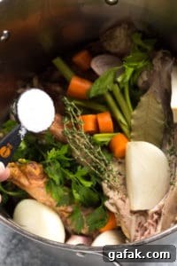 pouring salt into a large pot with turkey stock ingredients inside