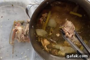 removing bones and veggies from a large pot of turkey broth into a container on the side