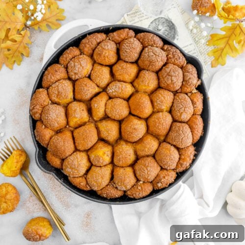 skillet pumpkin monkey bread on marble surface with yellow leaves, white pumpkin, and white flowers around.