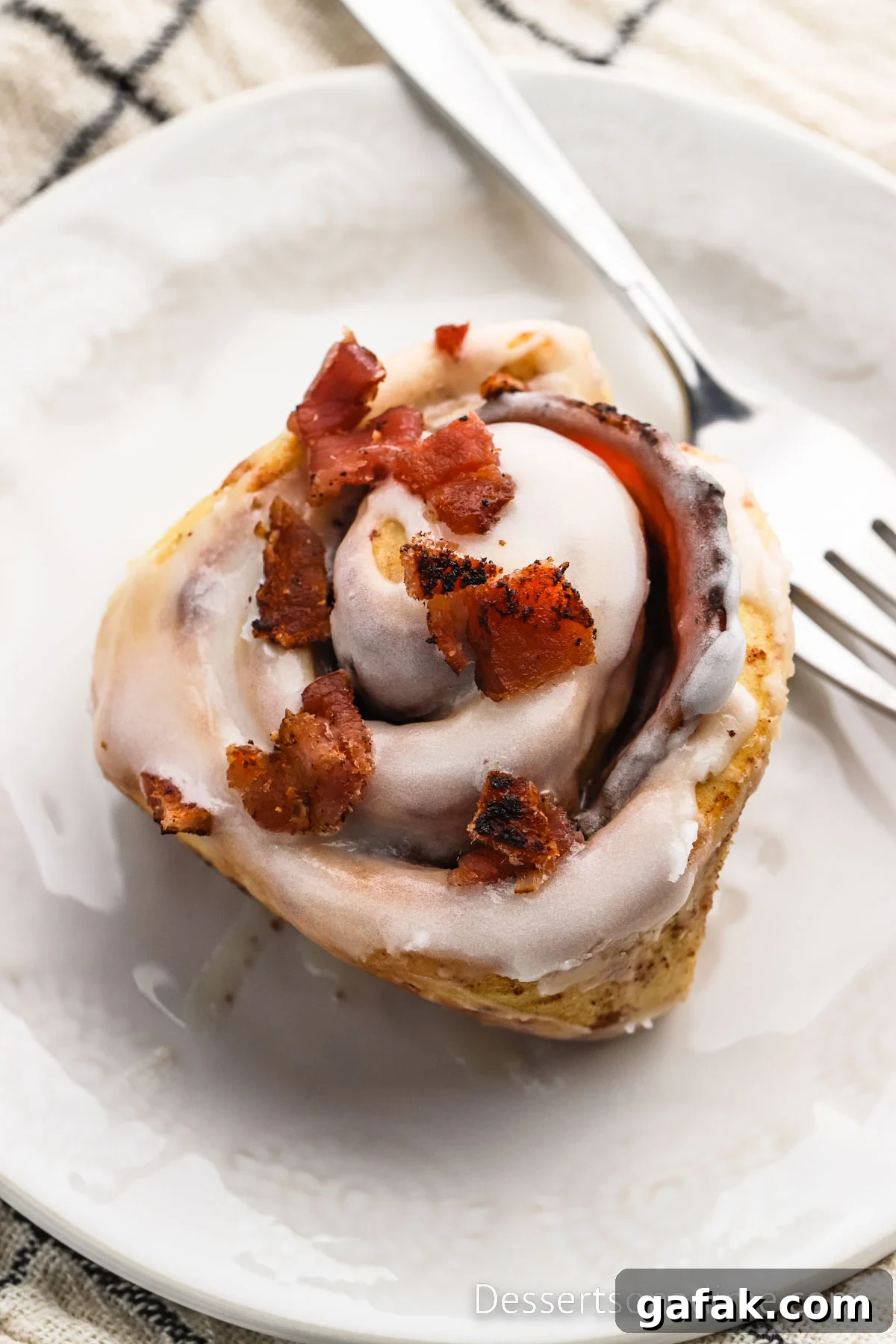 Bacon Cinnamon Roll on a plate beside a fork. 