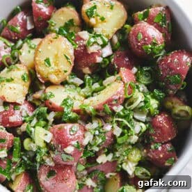 Potato salad with homemade mayo-free vinaigrette and fresh herbs in white bowl.