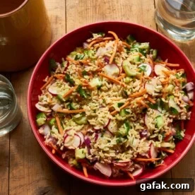 Vegetable and Brown Rice Salad with Honey Lemon Dressing in red bowl on table.