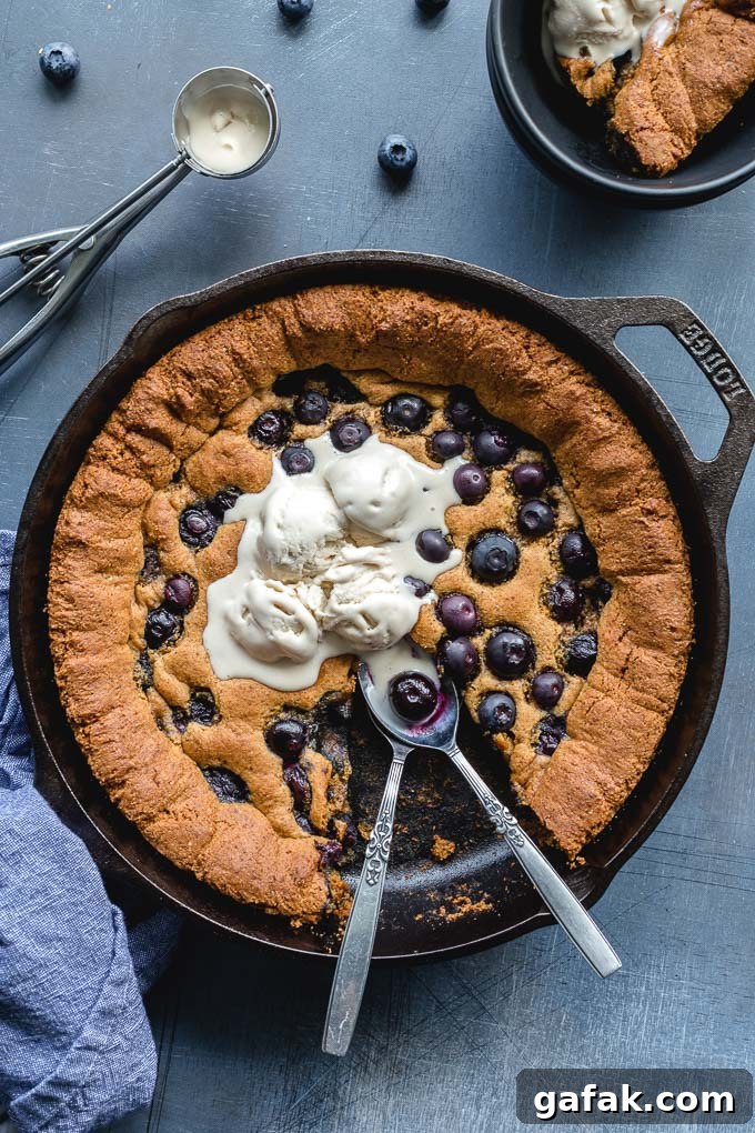 Overhead view of a blueberry skillet cookie topped with ice cream and a piece missing.
