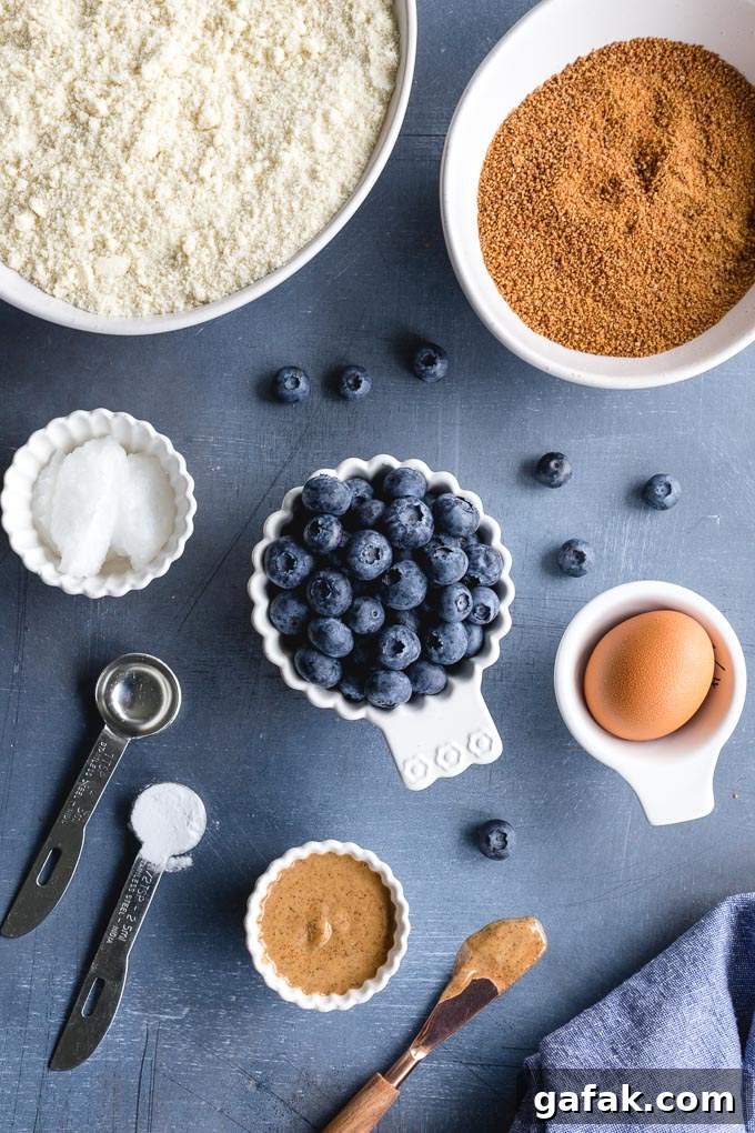 Ingredients to make an almond flour skillet cookie with blueberries arranged individually on a blue surface.