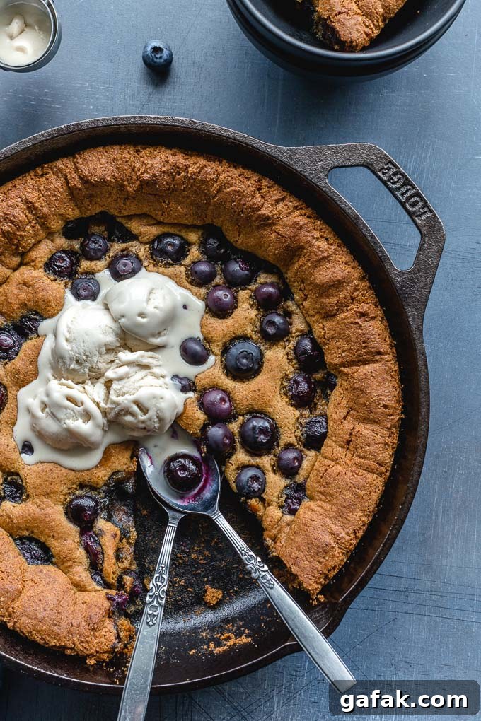 Up-close view of a skillet cookie with blueberries and ice cream.
