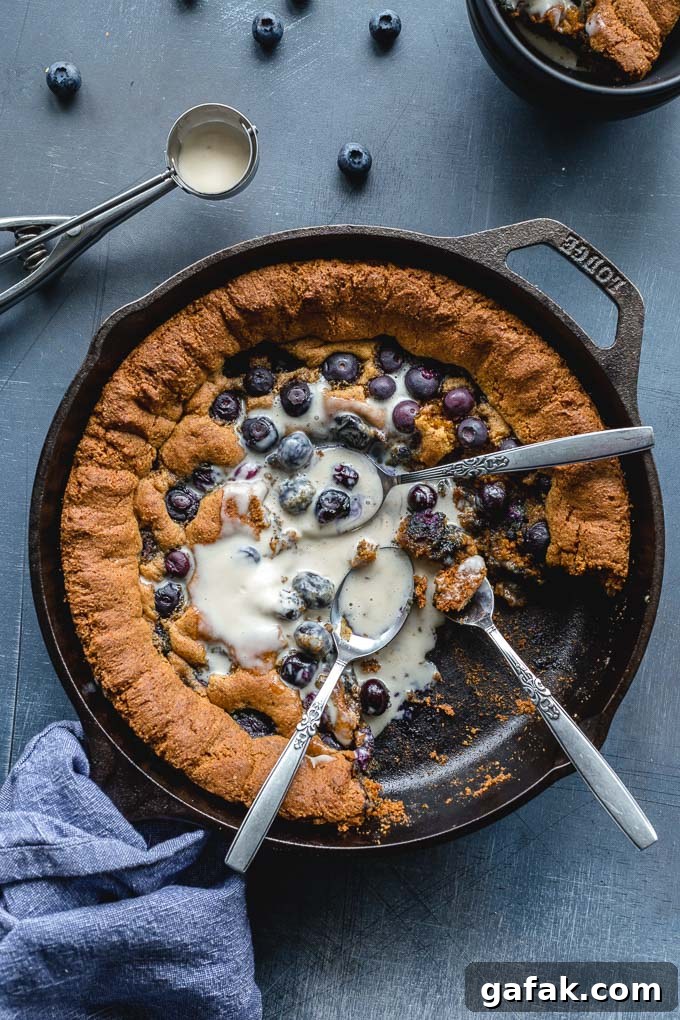 Overhead view of a giant blueberry cookie in a skillet with melted ice cream.