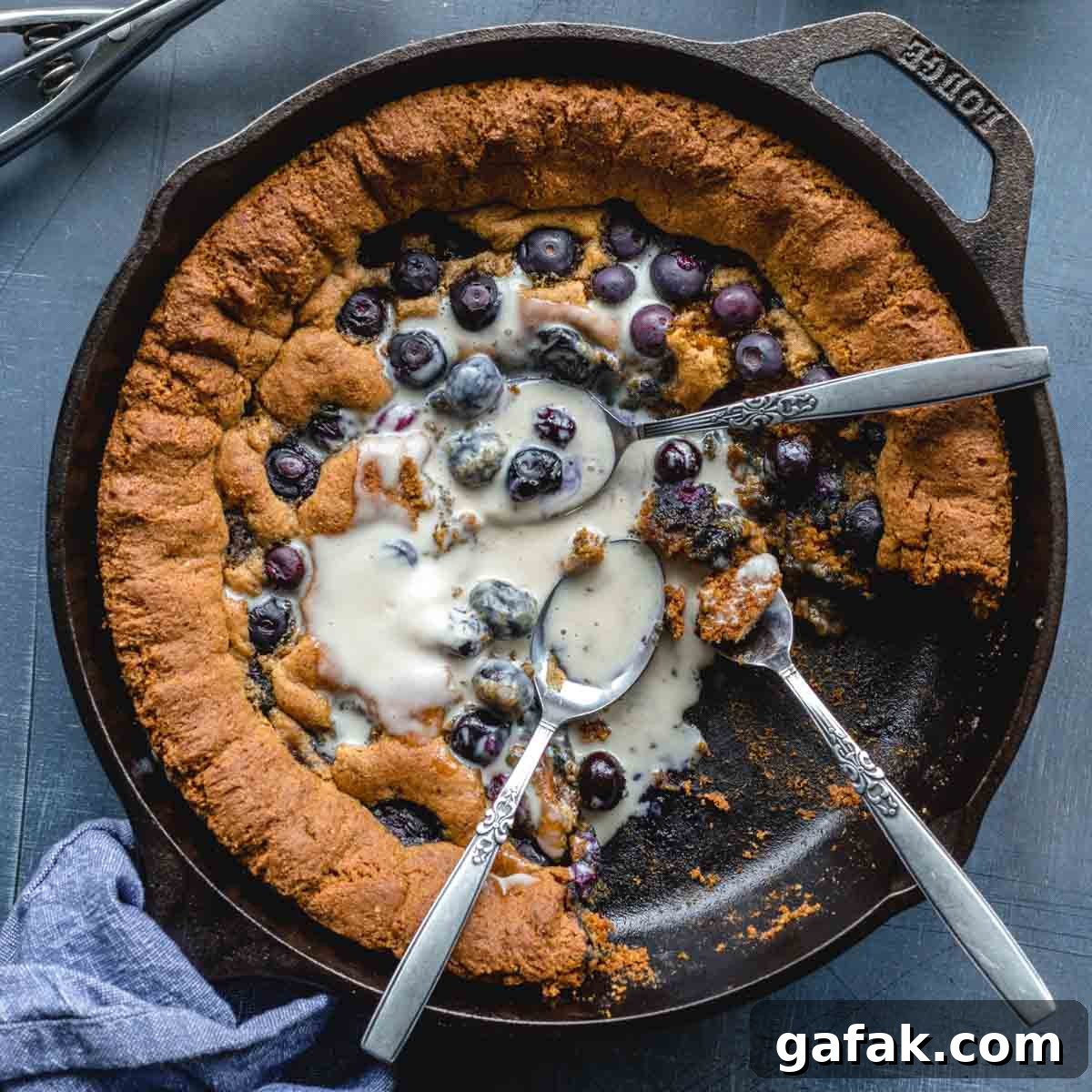 Overhead of a blueberry almond flour skillet cookie in a cast iron pan with spoons inserted and melted ice cream on top.