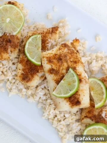 Air-fried cod topped with seasoning and slices of fresh lime on a white dish.