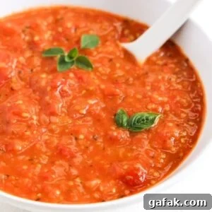 Cherry tomato sauce topped with two small basil leaves and a sprig of fresh oregano served in a white bowl with a white spoon.